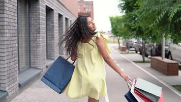 een aantrekkelijk jong meisje met lang donker haar- in een geel jurk verheugt zich na boodschappen doen met een mooi zo humeur. langzaam beweging. video