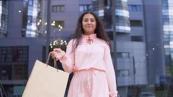 giovane bellissimo ragazza nel un' vestito dopo shopping con pacchi nel mani è contento acquisti. lento movimento. video