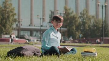 Online education, Back to school, Happy schoolboy, Learn lessons. Schoolboy teaches lessons while sitting on the grass near the school and looking at the camera video