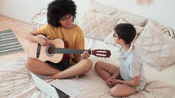 música enseñando, musical educación, jugando guitarra, hora juntos. afro americano niña enseñando niño a jugar guitarra utilizando ordenador portátil video