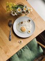 Fried eggs with chamomile flowers on a wooden table photo