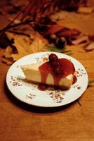 A piece of cake with cherry sauce on a plate and autumn leaves photo