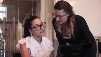 Close-up. Two beautiful young business women discuss a business project in the office using a mobile computer sitting at a table. video