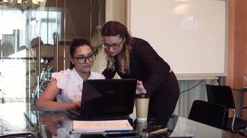 Two beautiful business women discuss a business project in the office using a mobile computer with a good mood. video