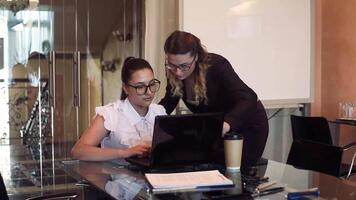 dos hermosa negocio mujer discutir un negocio proyecto en el oficina utilizando un móvil computadora. video