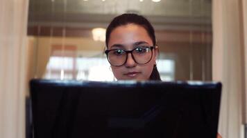ung skön företag kvinna i glasögon Arbetar använder sig av en mobil dator och mobil telefon Sammanträde på en tabell i de kontor med en Bra humör. närbild. hd. video