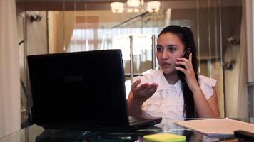 mooi jong bedrijf meisje met donker haar- in bedrijf kleren pratend Aan een mobiel telefoon in de kantoor zittend Bij de tafel video