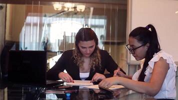 Due bellissimo attività commerciale donne discutere le difficoltà nel un' attività commerciale progetto nel un ufficio seduta a un' tavolo. HD video