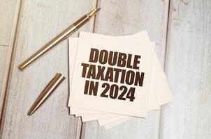 Card with DOUBLE TAXATION IN 2024 on wooden background. photo