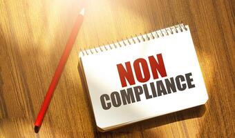 NON COMPLIANCE message on notepad with pencil on wooden background photo