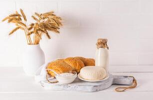 Fresh dairy products on a white wooden board and a vase with ears of corn on a wooden table. Concept of the Jewish holiday of Shavuot. Eco style photo