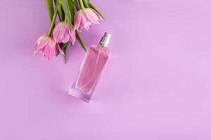 glass bottle of women's perfume or cosmetic spray on lilac background with spring flowers. Perfume and beauty concept. A copy space photo