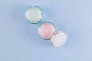 two beautiful glass cosmetic jars with delicate texture of face and body care cream on a blue background. Top view. A copy space. presentation. photo