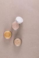 Three beautiful glass cosmetic jars with delicate texture of face and body care cream on a stone beige background. Top Vertical view. A copy space photo