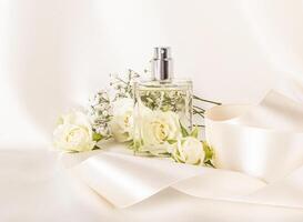 Elegant bottle of cosmetic spray, perfume on beige satin fabric with delicate roses and satin ribbon. Product presentation. Blank lay. photo