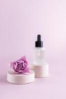 Fashion beauty product, serum in glass cosmetic bottle with dropper for face and body skin care standing on a round cement podium with a tulip flower photo