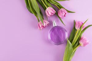 round glass bottle of women's perfume or cosmetic spray on lilac background with spring flowers. Perfume and beauty concept. A copy space. photo