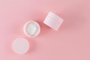 Two pink cosmetic jars with cosmetic self-care product on pink background. Open jar. Delicate white cream. A copy space. packaging. layout. Top view. photo