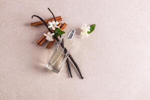An elegant transparent bottle with a delicate fragrance of women's perfume lies on the vanilla sticks and flowers. Top view. A copy space. photo