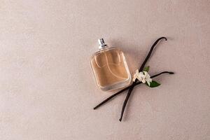 Glass bottle of perfume or cosmetic spray with natural vanilla scent on beige stone background with vanilla sticks. Top view. A copy space. photo