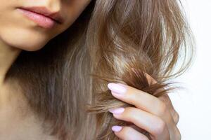 Cropped shot of a young beautiful woman holding a strand of hair in her hand and looking at her split ends. Isolated on a white background. Close up. Hair care concept. Beauty and health photo