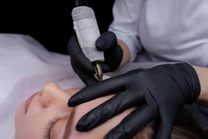 Completing permanent eyebrow makeup with a tattoo machine. PMU Procedure, Permanent Eyebrow Makeup. photo