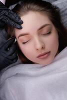 The master cleans the model's eyebrows from excess pigment after permanent makeup. PMU Procedure, Permanent Eyebrow Makeup. photo