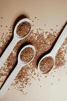 Flax seeds in wooden spoons on a beige background. photo