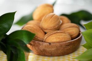 Bowl with tasty cookies and green leaves on table, closeup photo