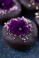 Chocolate truffles with violet flowers on a dark background. photo
