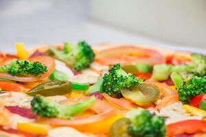 Vegetarian pizza with ham, pepper, tomato, onion, carrot, cucumber and broccoli photo