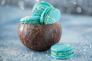 Tasty macaroons in coconut shell on blue background, closeup photo