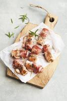 Grilled bacon wrapped in bacon on wooden cutting board over grey stone background. Top view, copy space photo
