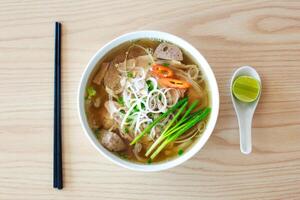 Thai style noodle soup with pork in bowl on wooden table photo