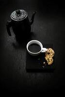 Cup of coffee and cookies on black table. Toned. photo