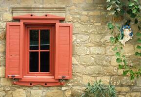 rojo ventana persianas y Roca pared con escultura foto