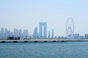 Clear blue sky over the modern skyline of Dubai, featuring the iconic Ferris wheel and unique skyscrapers. Dubai, UAE - August 15, 2023 photo