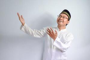 Asian Muslim man wearing glasses and white cloth pointing up pose for ramadhan and eid al fitr. Isolated white background photo