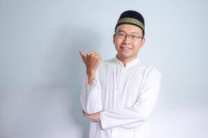 Asian Muslim man wearing glasses and white cloth smiling and pointing pose for ramadhan and eid al fitr. Isolated white background photo