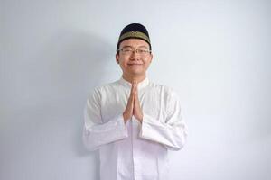 asiático musulmán hombre vistiendo lentes y blanco paño sonriente haciendo saludo actitud para ramadhan y eid Alabama fitr. aislado blanco antecedentes foto