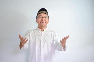 Asian Muslim man wearing glasses and white cloth smiling doing greeting pose for ramadhan and eid al fitr. Isolated white background photo