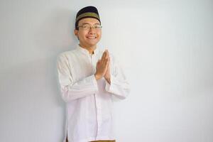 Asian Muslim man wearing glasses and white cloth smiling doing greeting pose for ramadhan and eid al fitr. Isolated white background photo