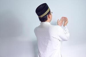Asian Muslim man wearing glasses and white cloth praying back side pose for ramadhan and eid al fitr. Isolated white background photo
