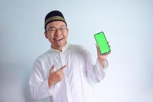 Asian Muslim man wearing glasses and white cloth pointing phone pose for ramadhan and eid al fitr. Isolated white background photo