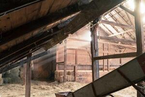 luz de sol rayos y ligero vigas dentro un antiguo rústico de madera granero con heno fardos y Paja en un granja foto