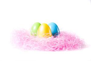 Three Colorful Easter Eggs On A Bed Of Pink Grass On White Background photo