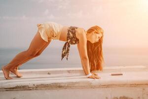 Woman park yoga. Side view of free calm bliss satisfied woman with long hair standing in morning park with yoga position against of sky by the sea. Healthy lifestyle outdoors in park, fitness concept. photo