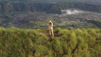 Aerial view of man with a camera on top of a cliff overlooking the mountains. Cameraman looks at the sunrise on the volcano Batur on the island of Blai in Indonesia. video