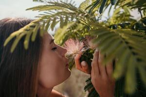 Beauty portrait of happy woman closeup. Young girl smelling Chinese acacia pink blossoming flowers. Portrait of young woman in blooming spring, summer garden. Romantic vibe. Female and nature photo