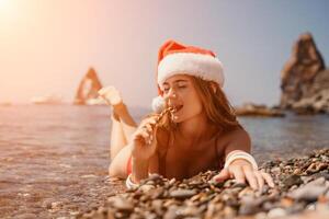 mujer viaje mar. contento turista disfrutar tomando imagen en el playa para recuerdos. mujer viajero en Papa Noel sombrero mira a cámara en el mar bahía, compartiendo viaje aventuras viaje foto